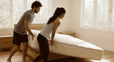 A man and woman rotate the mattress on a bedframe